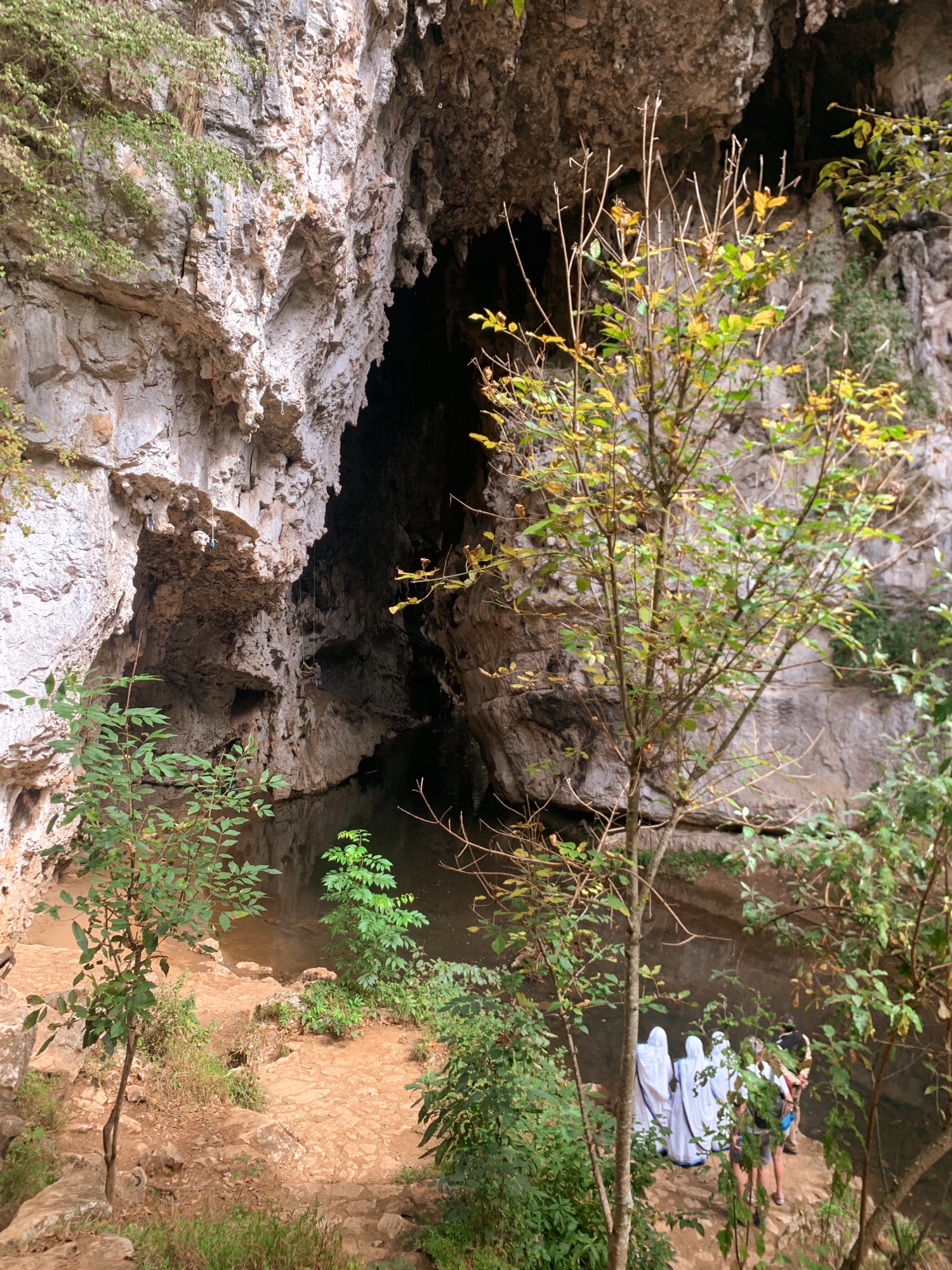 Large rock formation of an arch, river running through it and four people in white cloaks doing a prayer