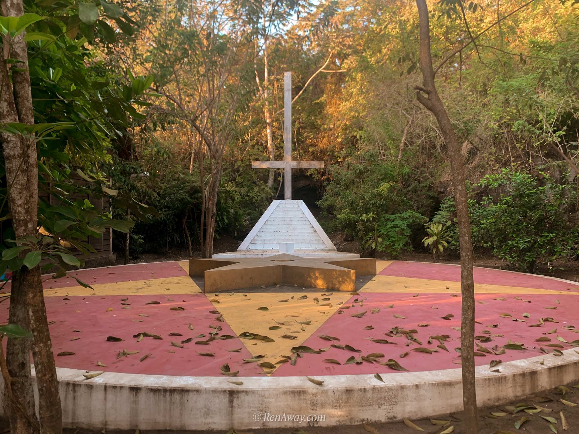 a concrete podium with a pentagon in red and yellow and an upside down cross where black masses are held. it is surrounded by trees and there are leaves on the concrete. this is in catemaco, mexico, a town known for witchcraft and dark tourism